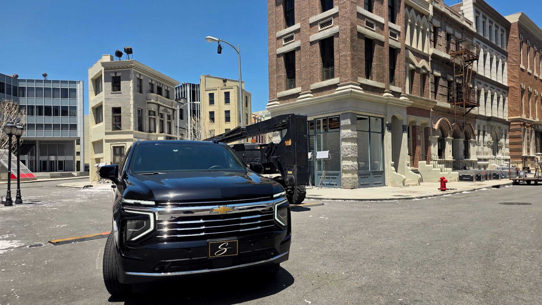 Black Chevrolet Suburban with a Signature S plate, parked on a Hollywood studio backlot street
